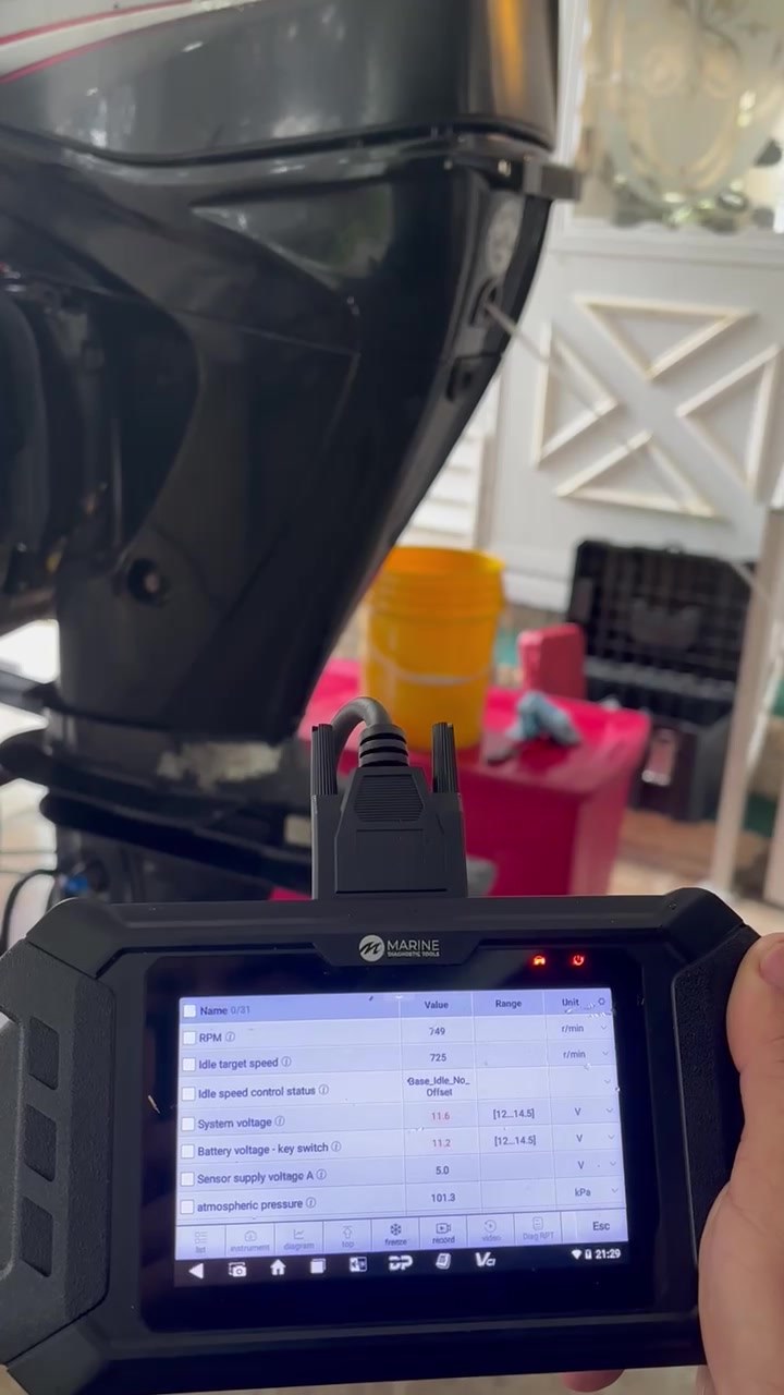 Diagnostic scan tool plugged into a Mercury FourStroke outboard, showing live engine readings in the customer's driveway